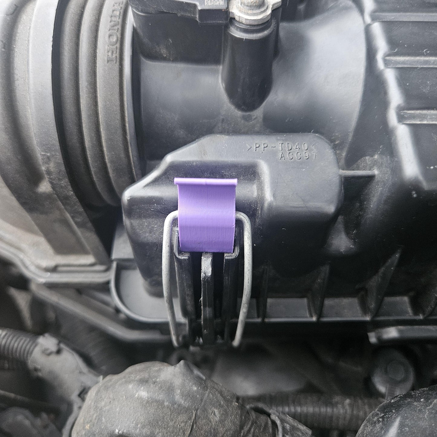 Close-up of 3D printed Honda air cleaner clip in purple attached to black air cleaner housing